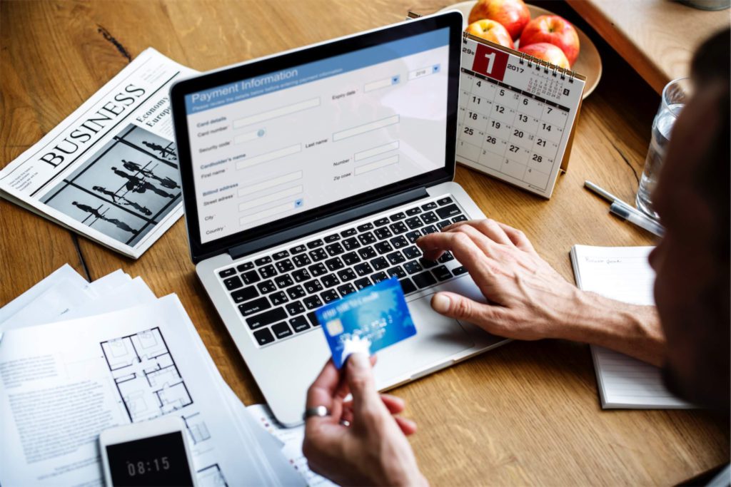 man holding a credit card and keying payment details into laptop