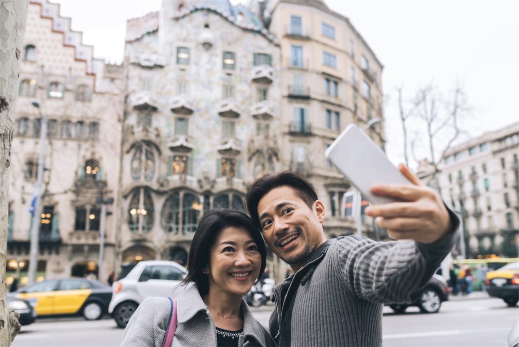 A couple taking a selfie at the roadside, with old buildings in the background